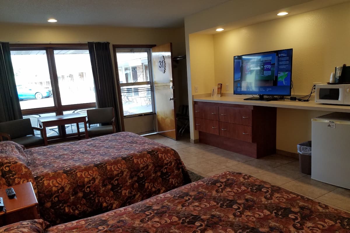 A hotel room with two beds, a television, a refrigerator, a desk, and a window with curtains.