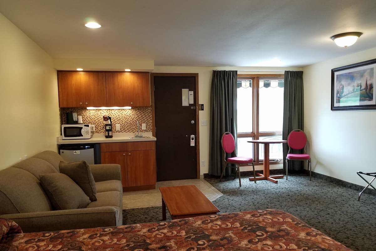 A compact hotel room with a kitchenette, a sofa, a small table, and a dining area with two chairs.