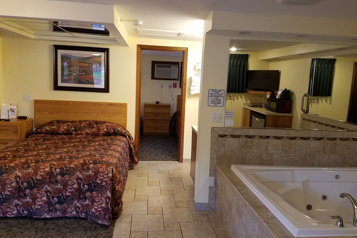 A hotel room with a bed, a bathroom with a bathtub, a television, and a framed picture on the wall.