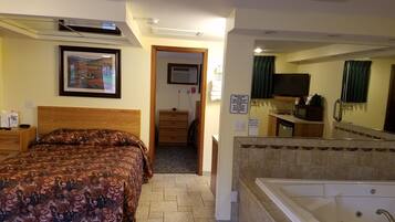 Quarto de hotel com cama, banheiro com banheira, televisão e quadro na parede.