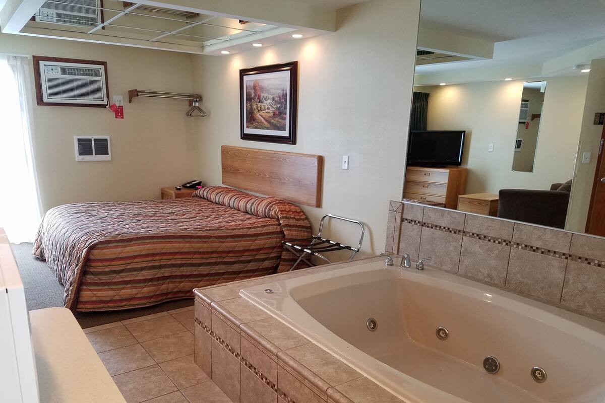 A hotel room with a large bed, a separate bathroom with a bathtub, and a flat-screen TV.