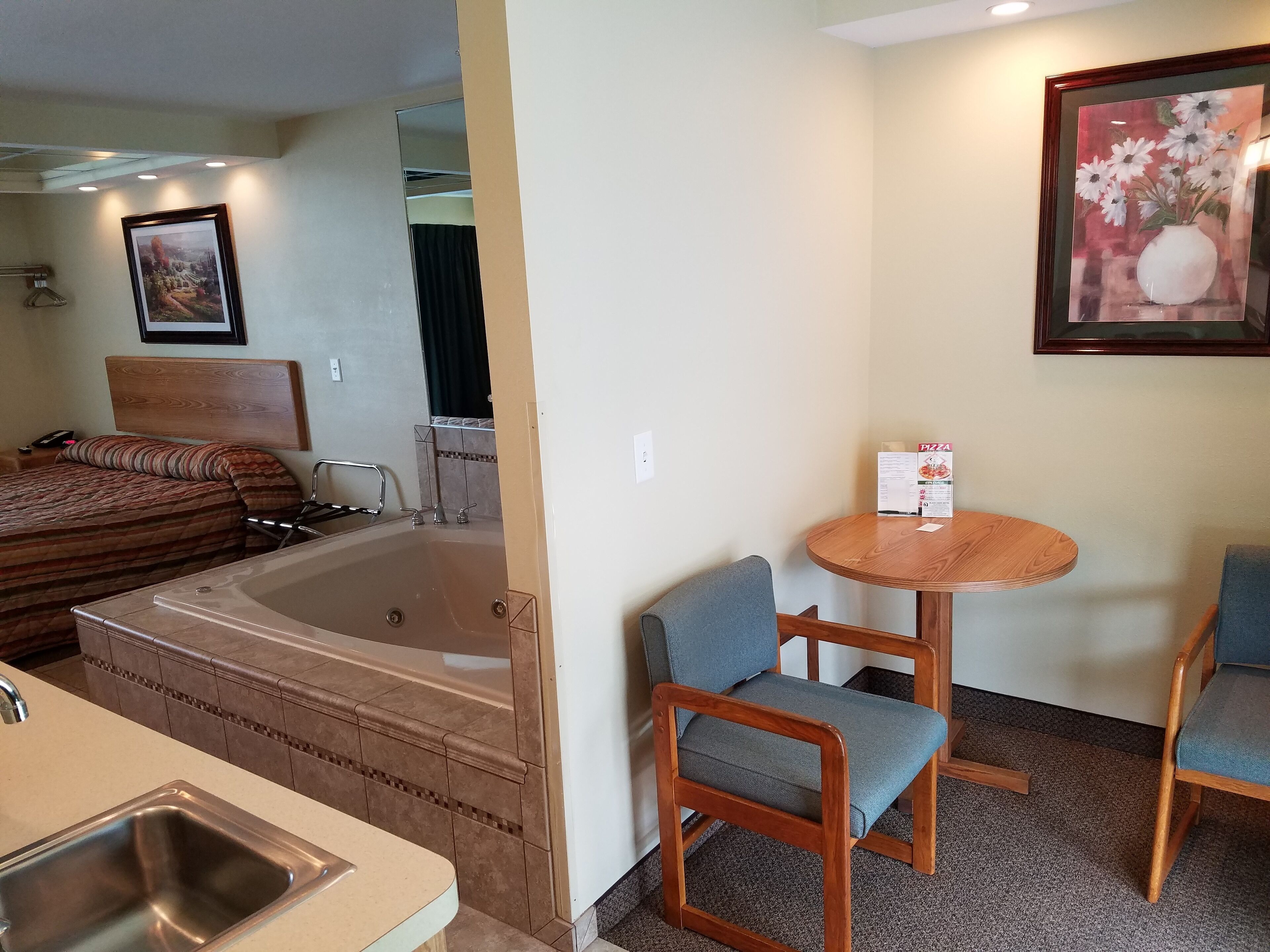 Quarto de hotel com uma banheira grande, uma mesa de jantar com cadeiras, uma pequena cozinha e um quadro na parede.