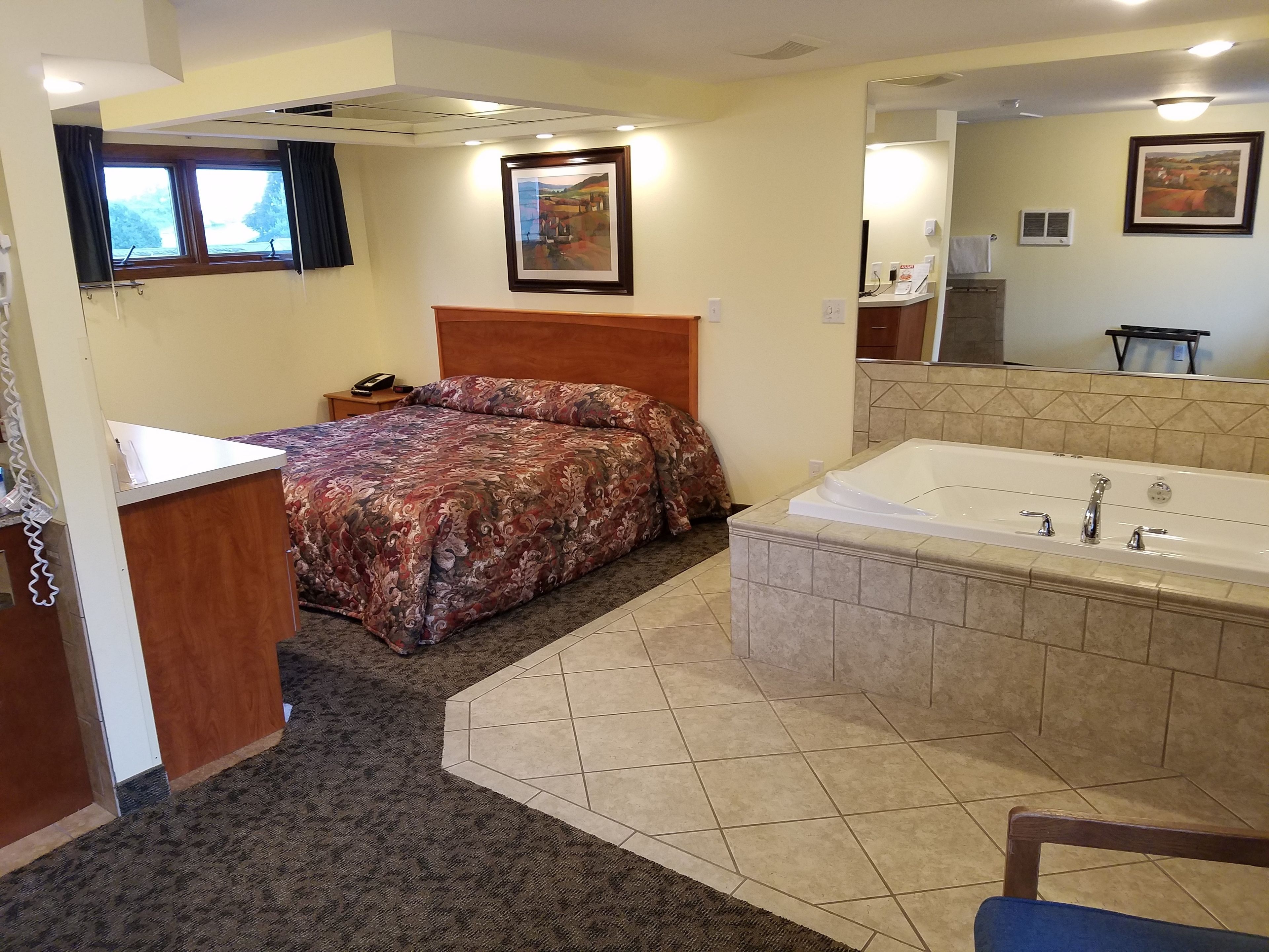 A hotel room with a bed, a bathroom with a bathtub, and a desk with a telephone.