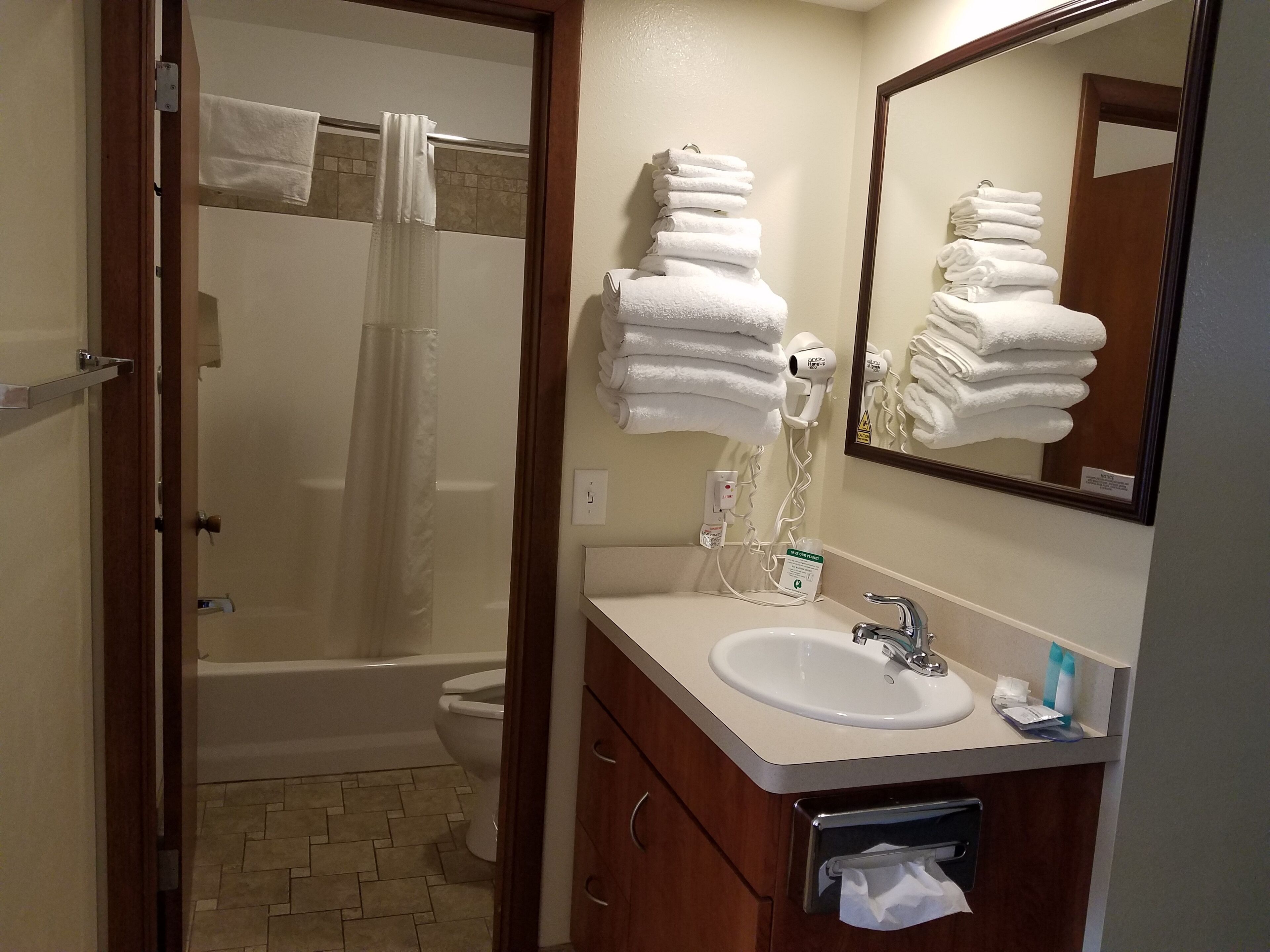 A bathroom with a shower, toilet, sink, and a stack of white towels.
