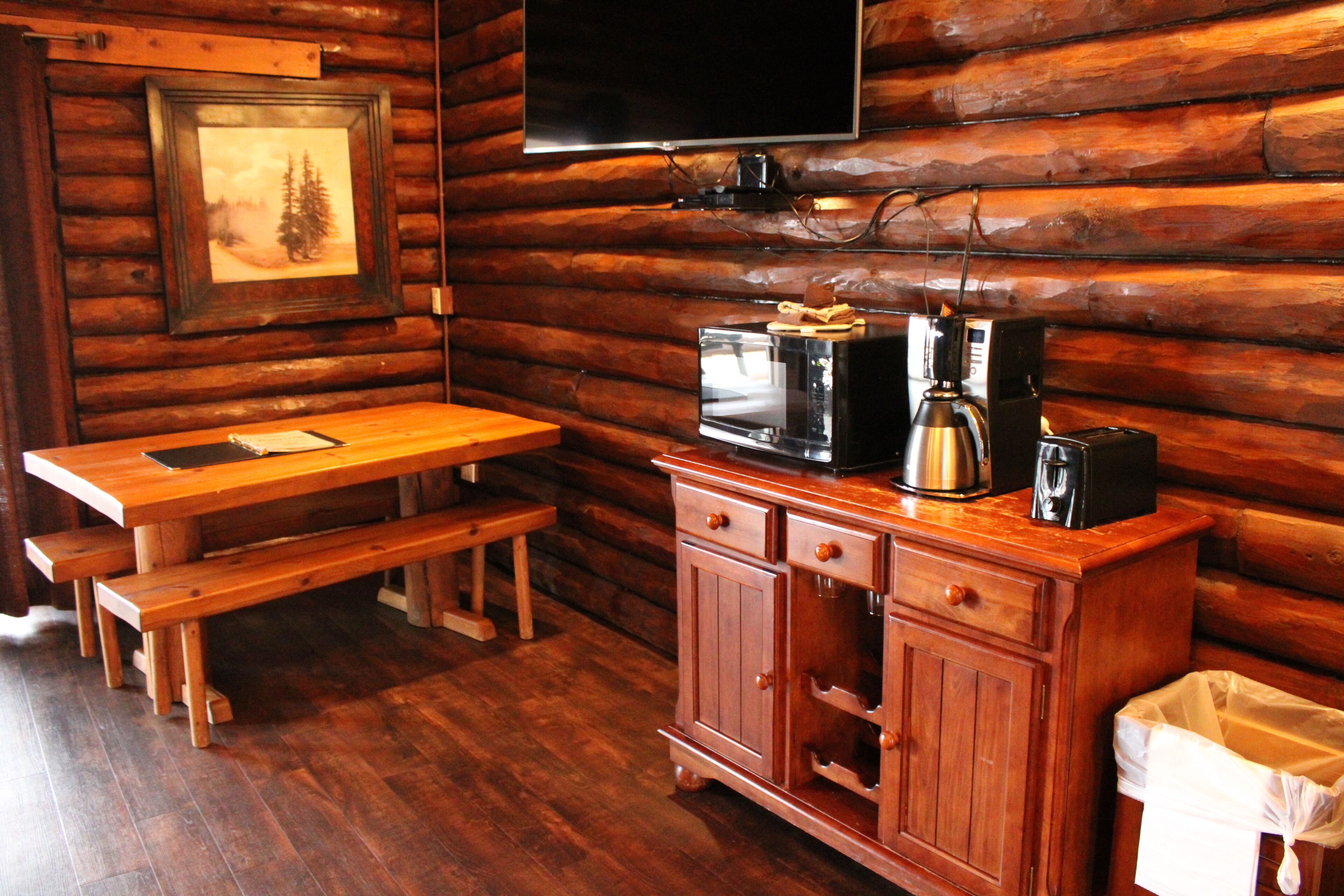 A wooden cabin interior with a wooden table, bench, and a cabinet with a coffee maker.