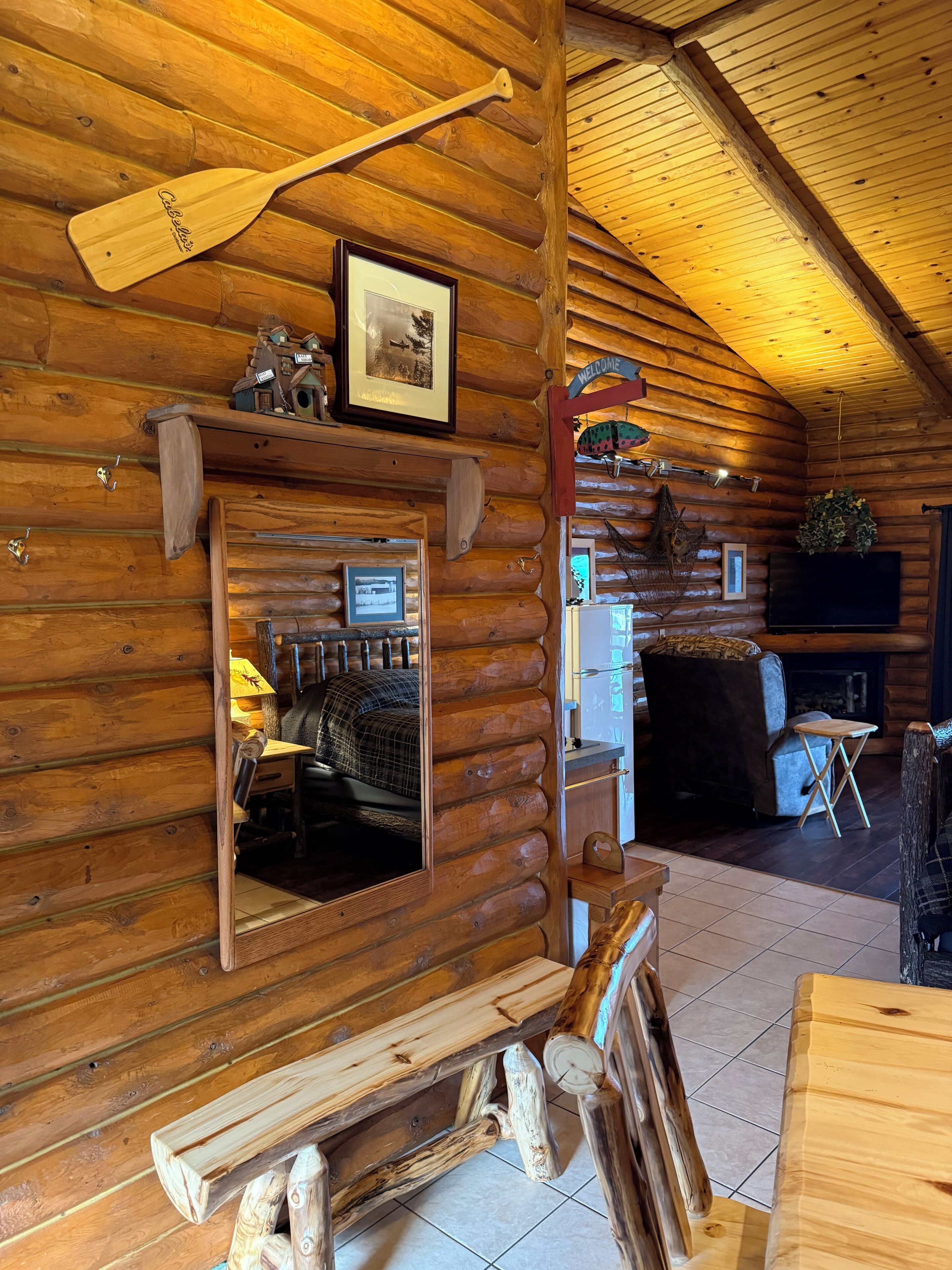 A log cabin interior with a wooden dining table, a fireplace, and a mirror reflecting the room.