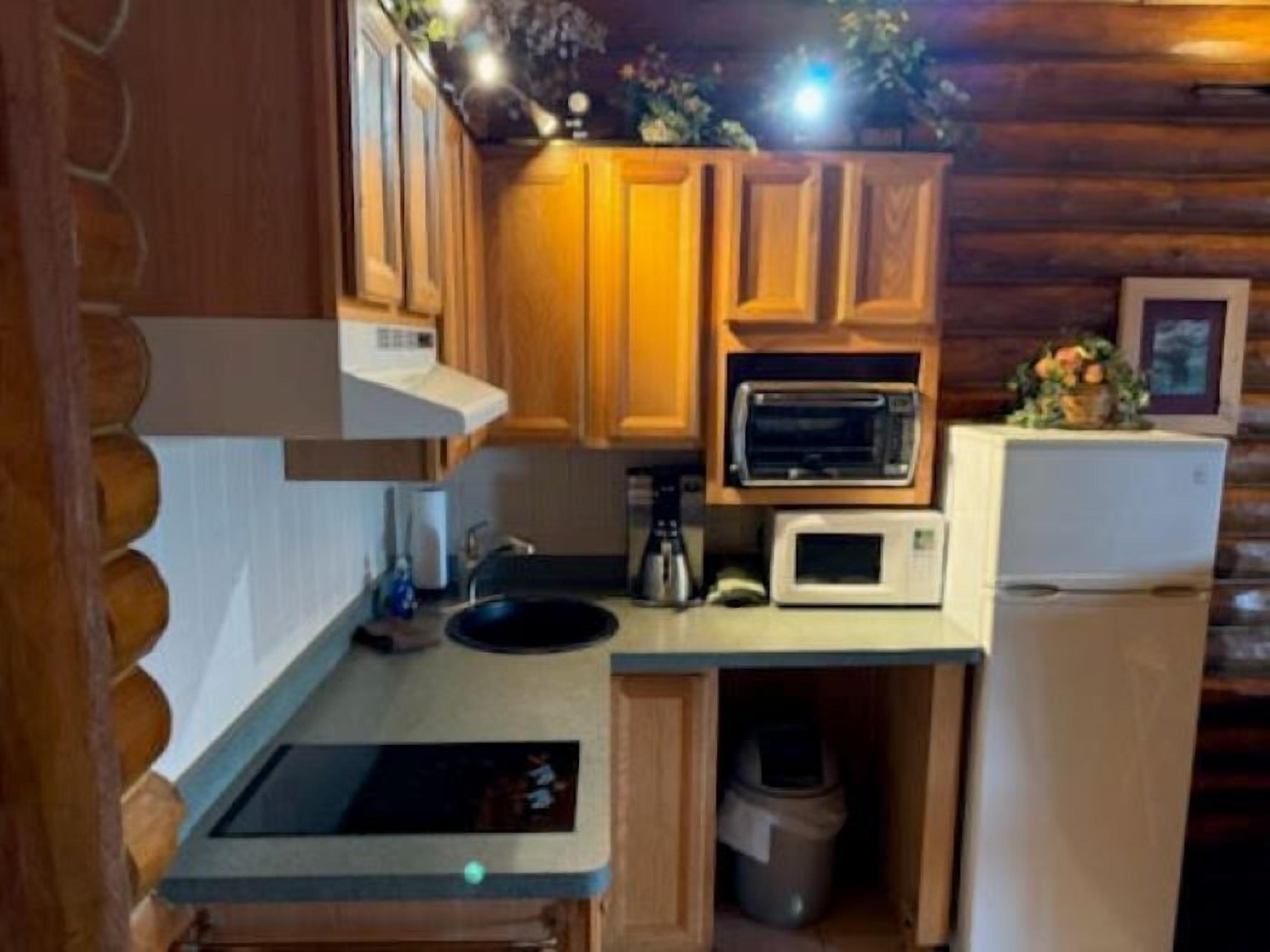 A compact kitchen with wooden cabinets, a microwave, a sink, and a trash bin.