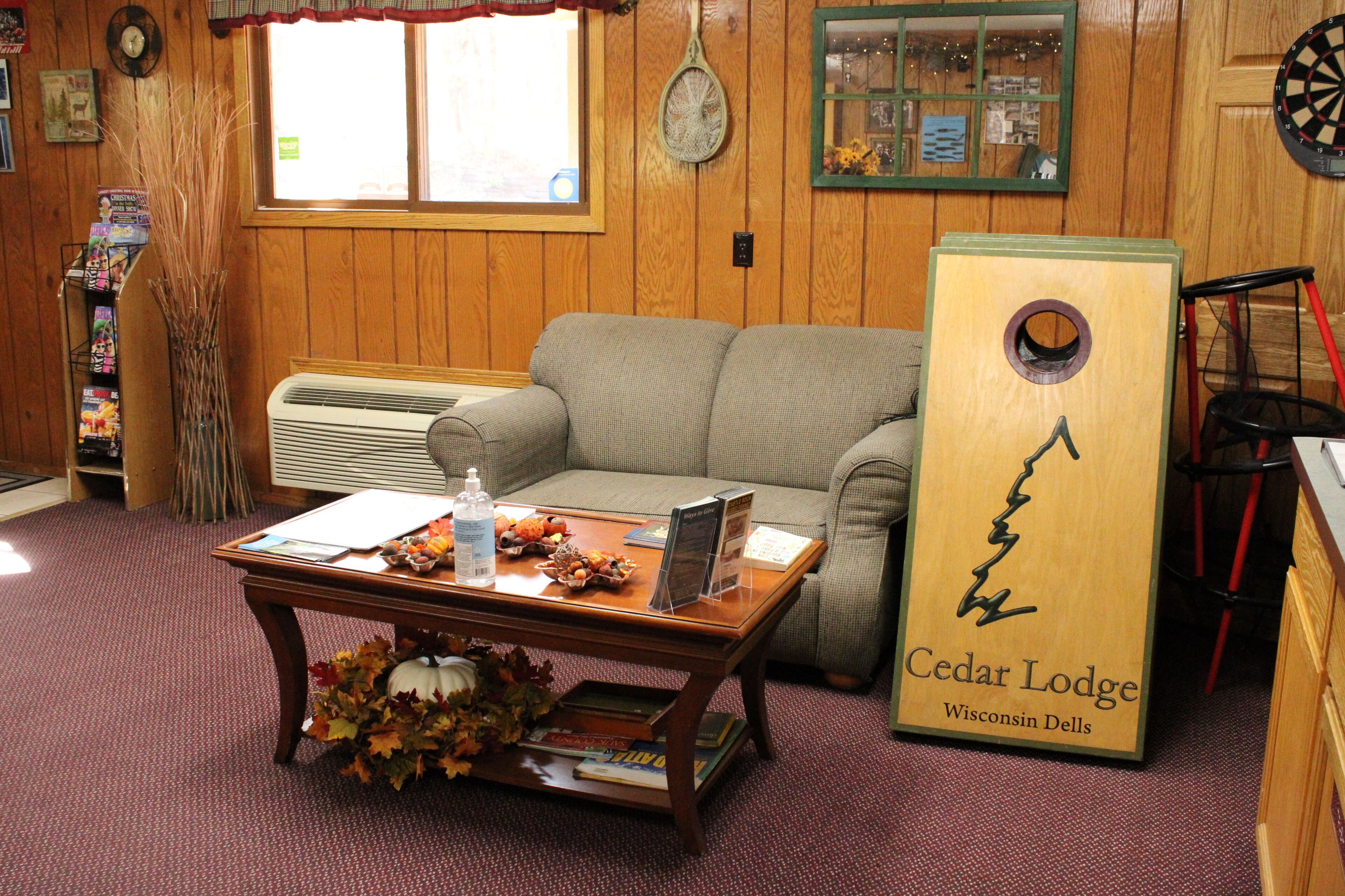 A cozy room with a wooden interior, a sofa, a coffee table with books and a water bottle, and a sign for Cedar Lodge Wisconsin Dells.