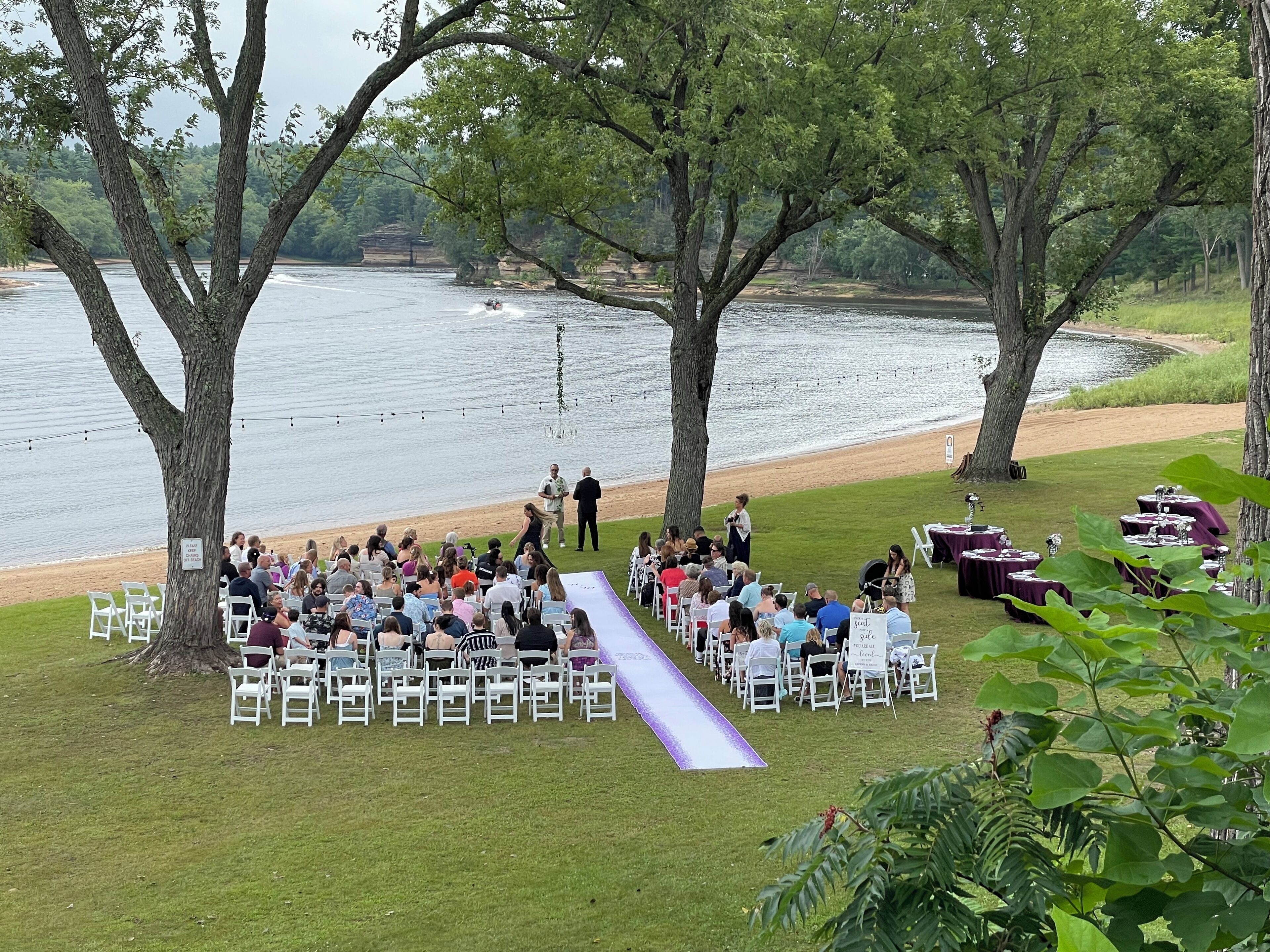 An outdoor wedding ceremony with guests seated on white chairs facing a stage.