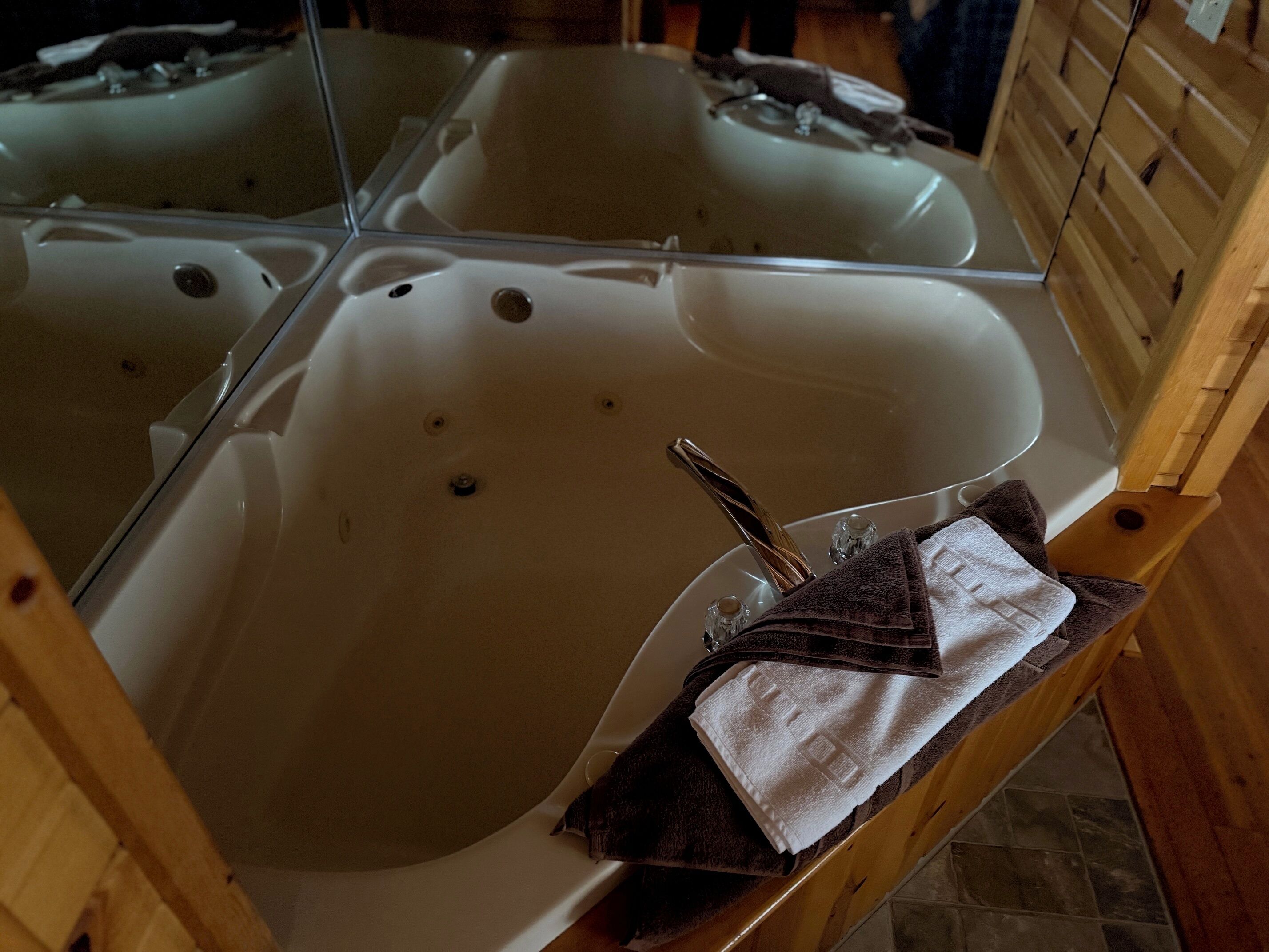 Une salle de bain avec une grande baignoire, un miroir et une chaise en bois sur laquelle est posée une serviette.