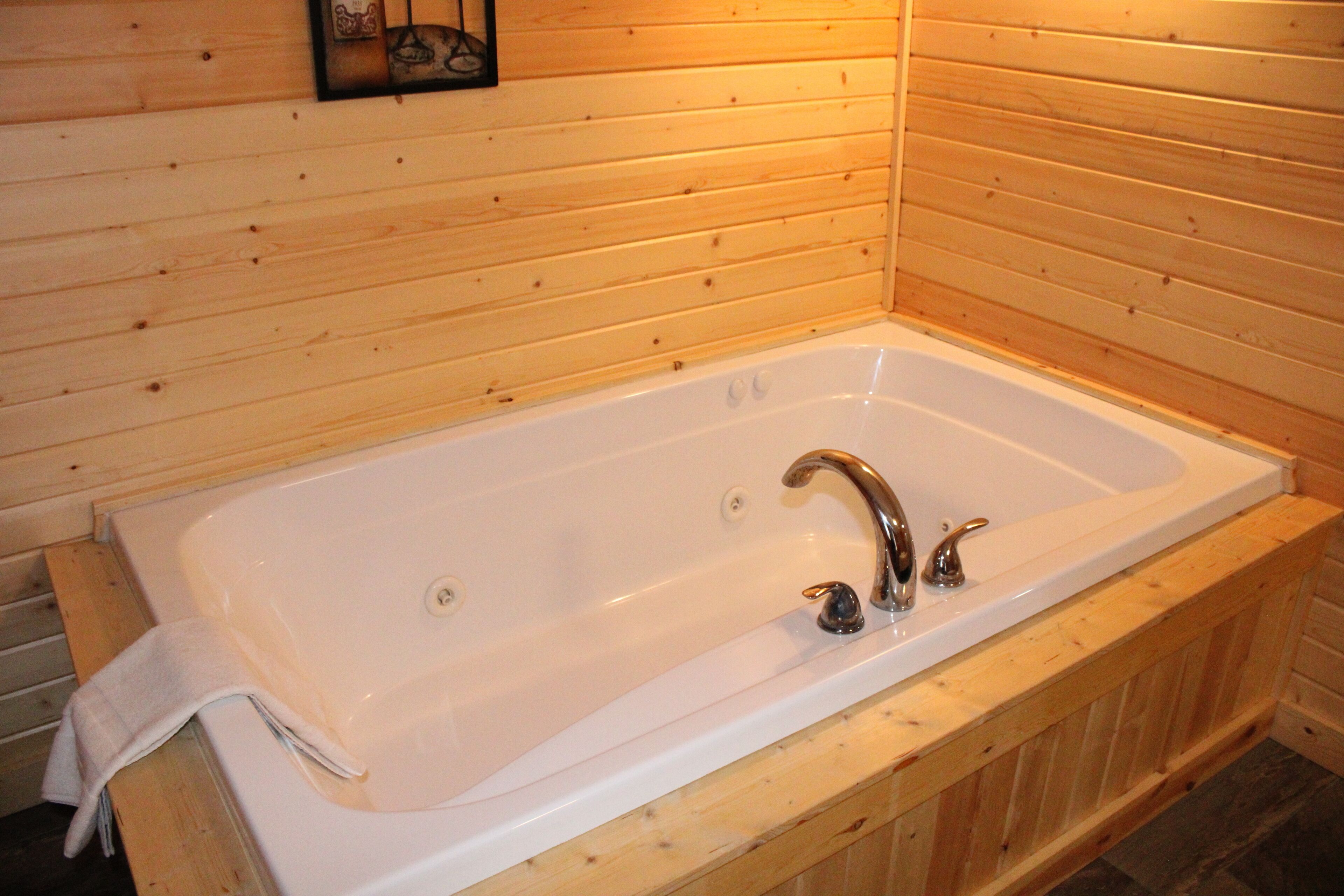 A wooden cabin with a white bathtub, wooden walls, and a small framed picture on the wall.