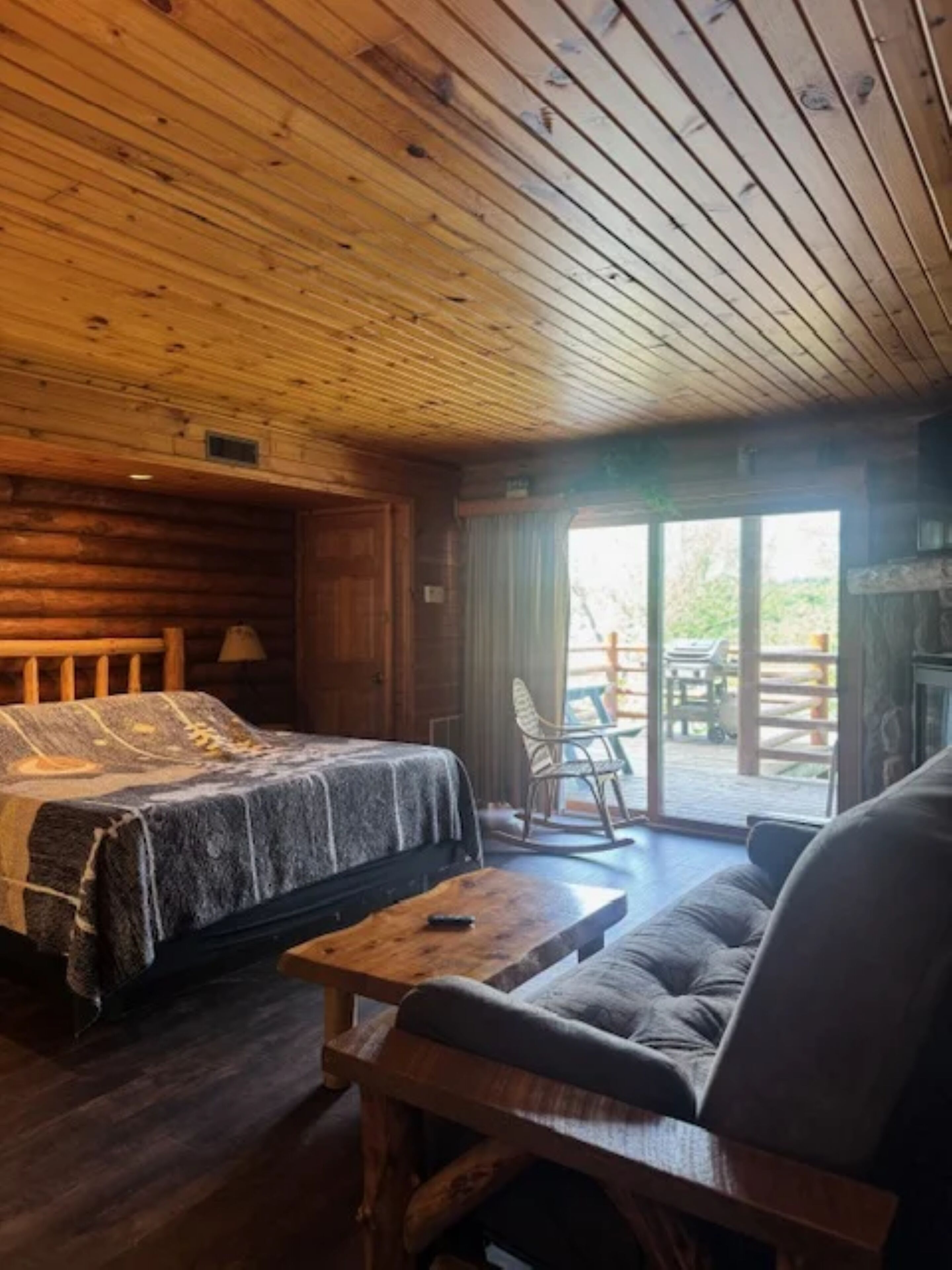 Une pièce chaleureuse dans un chalet en rondins, avec un lit, un canapé, une table en bois et un fauteuil à bascule.