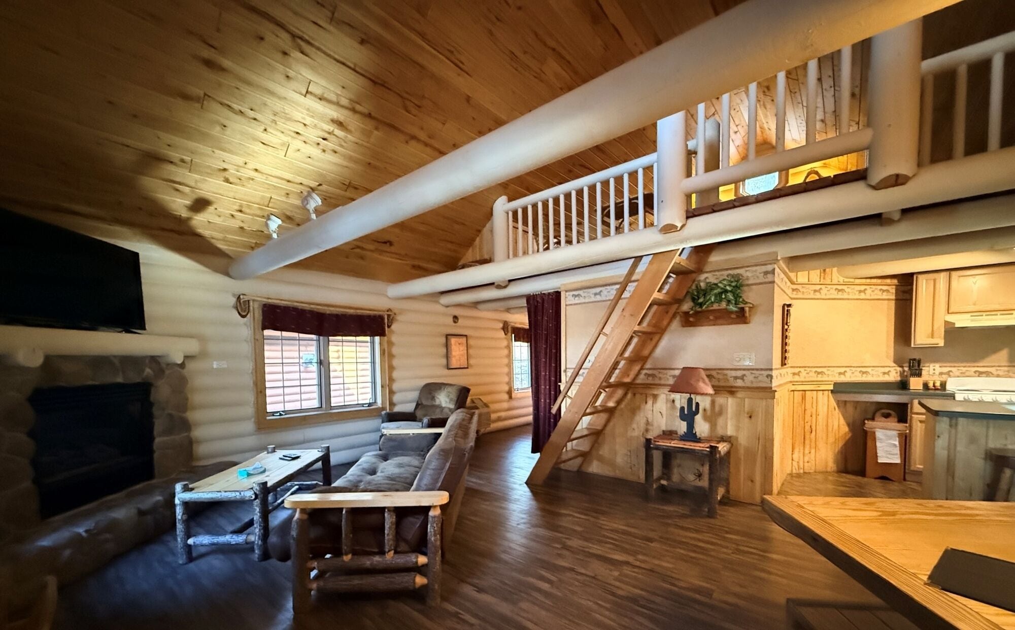 A log cabin interior with a loft bedroom, a dining area, and a kitchen.