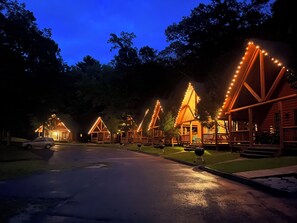 Une rangée de chalets en rondins, illuminés de guirlandes lumineuses, une allée pavée et une pelouse.