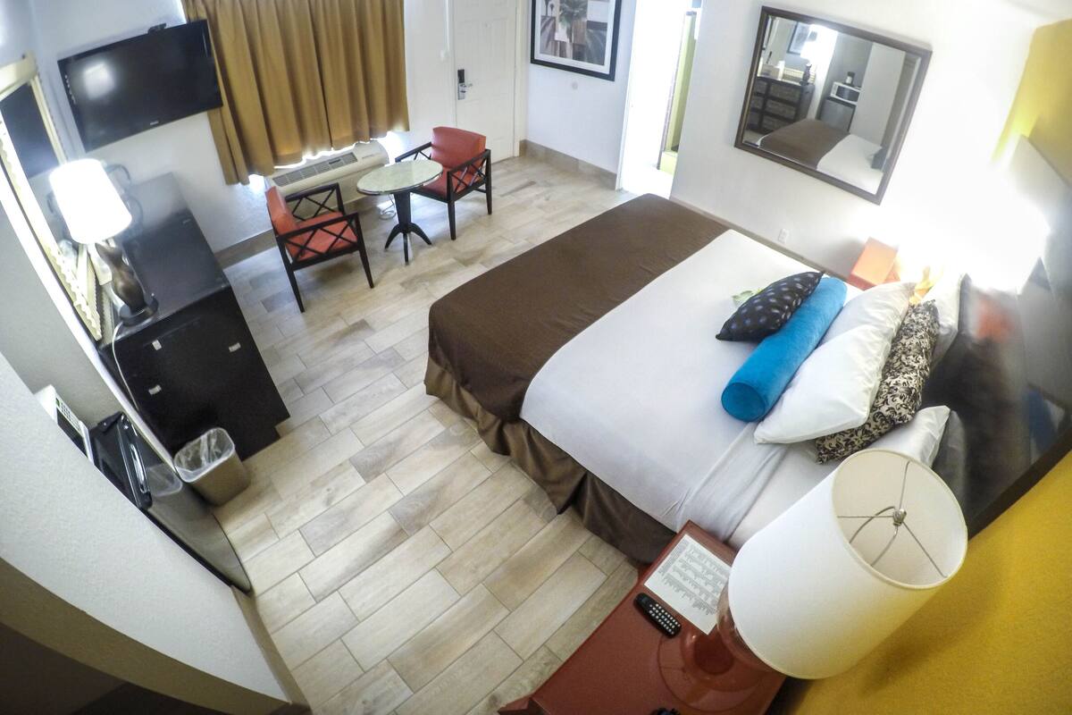 A hotel room with a bed, a desk, a chair, a TV, and a window with curtains.