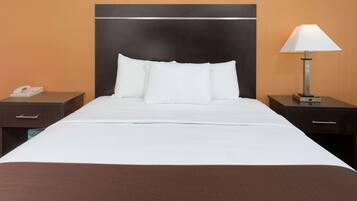 Ein Hotelzimmer mit einem großen Bett, weißer Bettwäsche, einem dunklen Kopfteil, einer Nachttischlampe und einem Nachttisch mit Telefon.