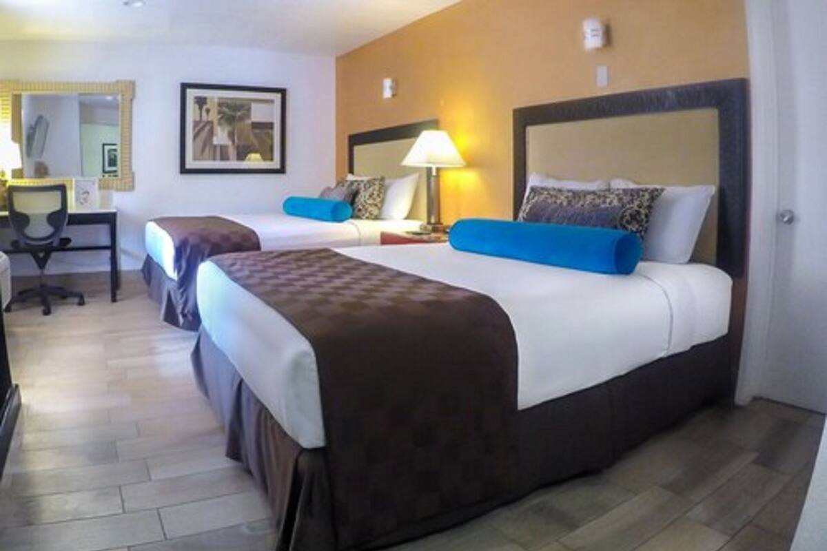 A hotel room with two beds, a desk, and a chair.