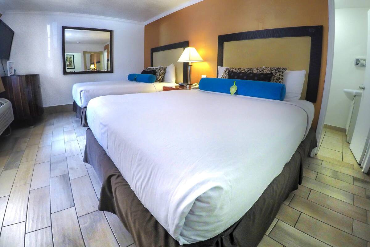 A hotel room with two beds, a large mirror, a bedside lamp, and a small table.