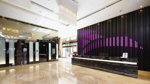 Un hall d’hôtel moderne avec un sol en marbre poli, un comptoir d’accueil surmonté d’une plaque de marbre noir et un mur décoratif orné de lignes verticales.