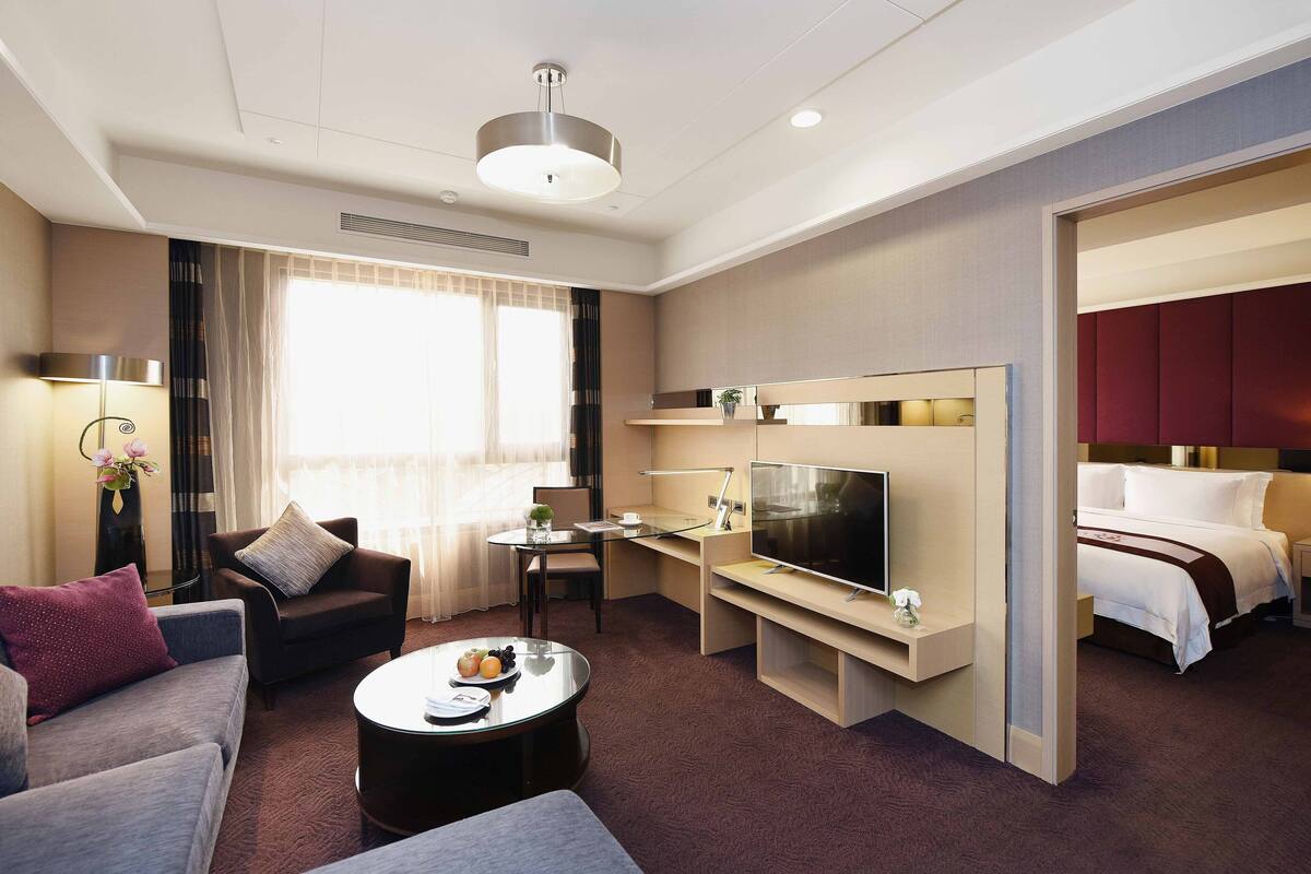 Ein modernes Hotelzimmer mit Sofa, Sessel, Fernseher, Nachttisch und Bett.