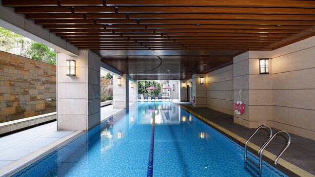 Une piscine dotée d’un plafond en bois et de murs carrelés, entourée d’un mur de pierre et d’une barrière en verre.