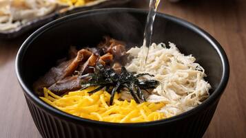 A bowl of food with various ingredients, including shredded cheese, seaweed, and meat, being poured into it.