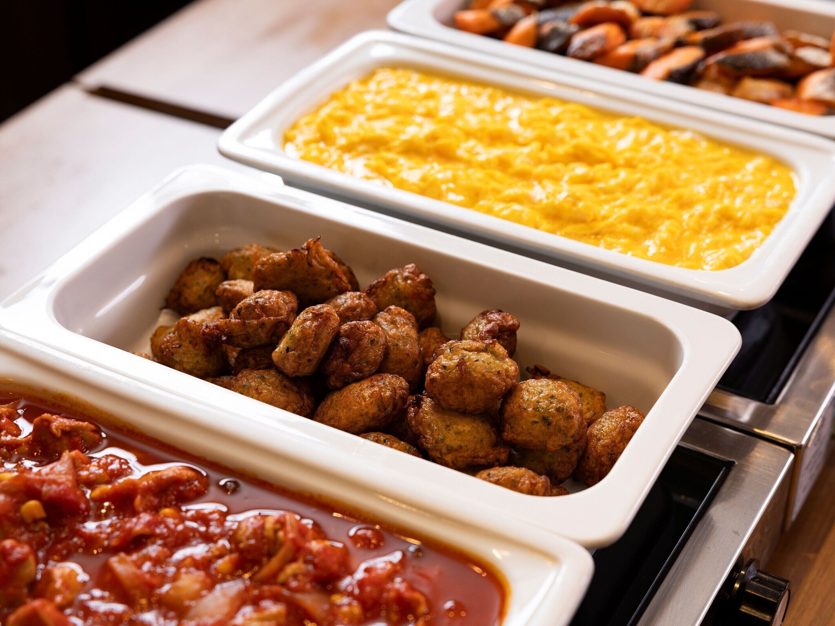 A buffet with various dishes including meatballs, a yellow sauce, and a red sauce.