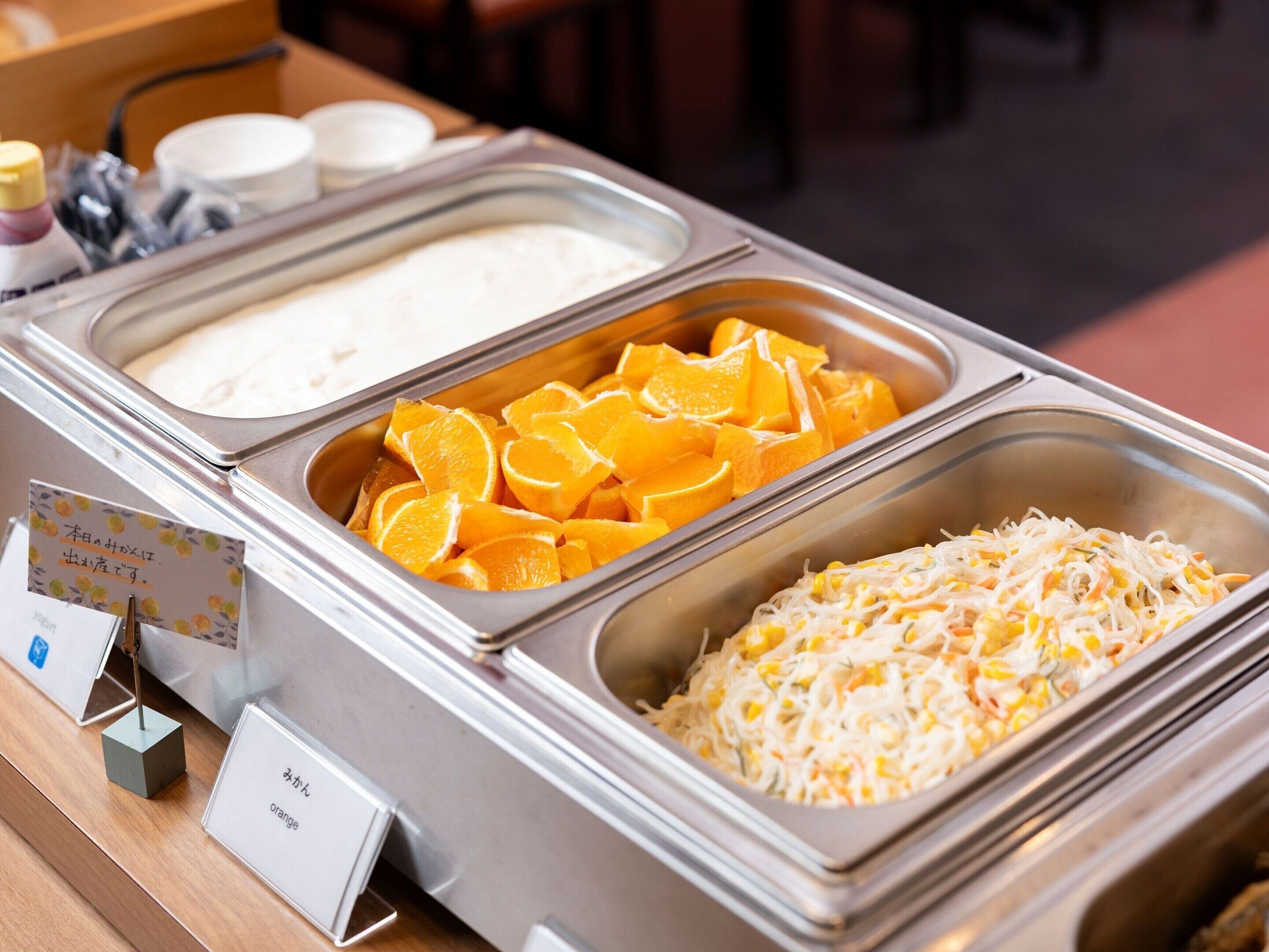 Un buffet composé de trois types de plats : un plat de riz blanc, des tranches d’orange et une salade de nouilles.