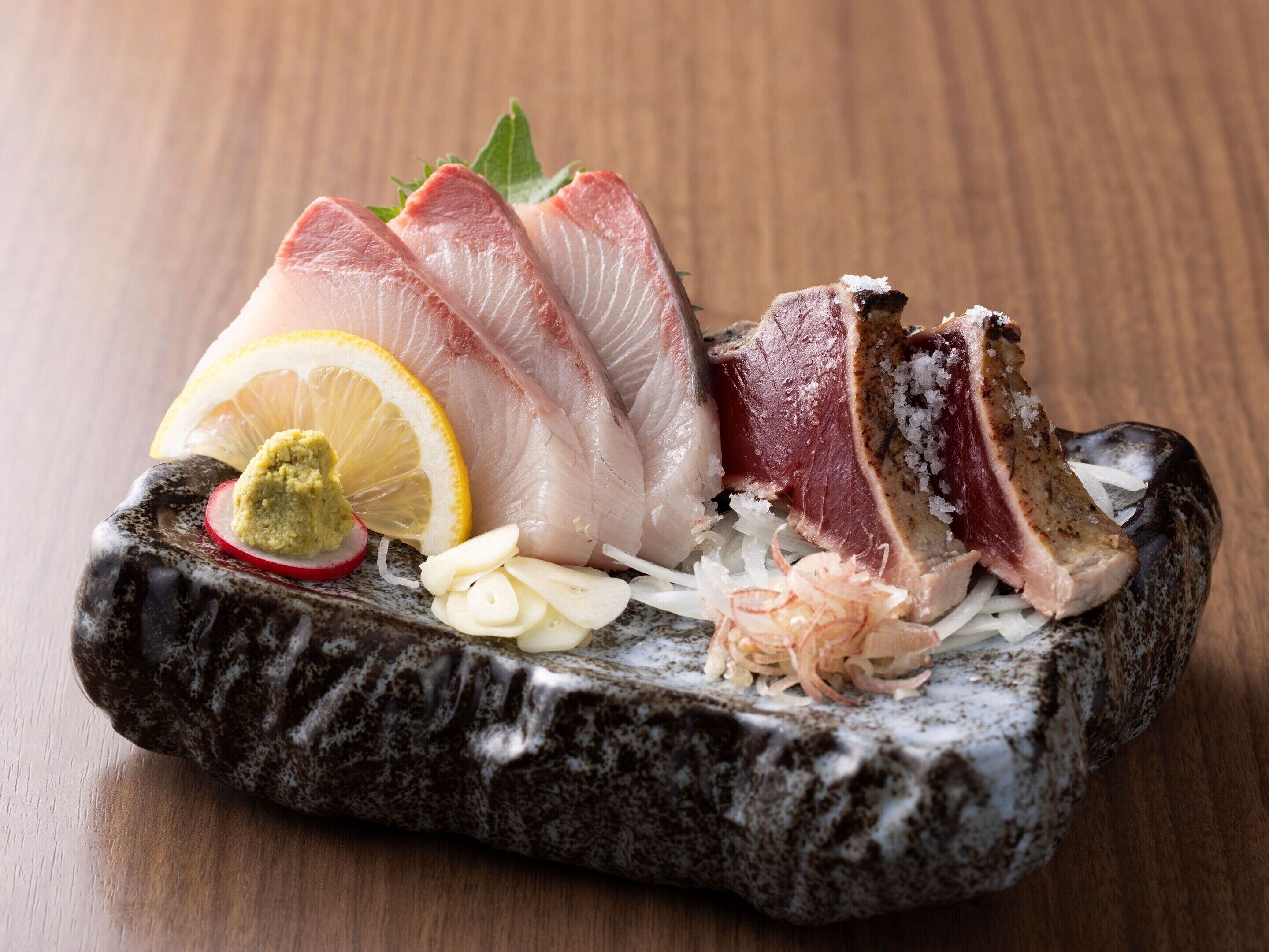 A stone serving dish with sashimi, lemon, wasabi, and pickled ginger.