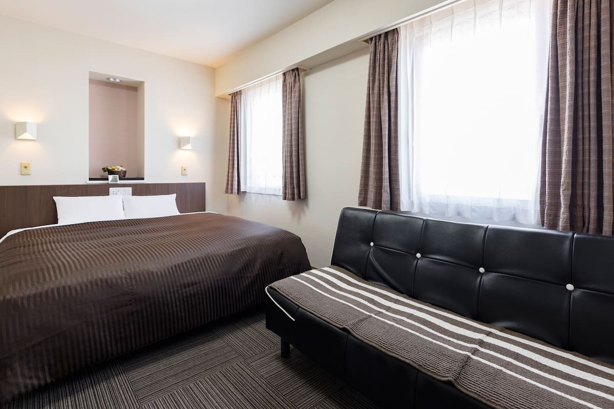 Una habitación de hotel con cama, sofá, ventana con cortinas e iluminación en la pared.