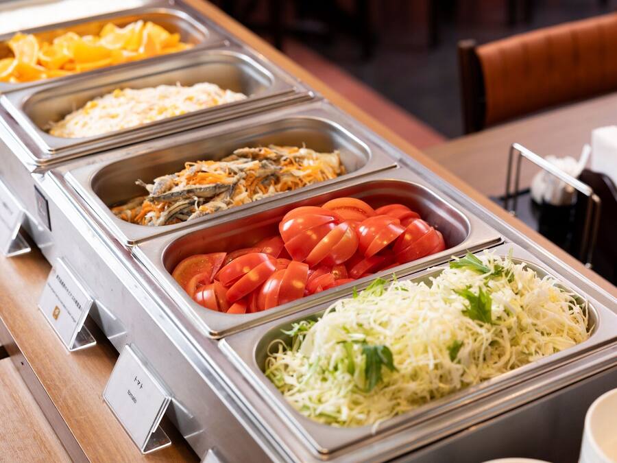 A buffet with various food options including sliced tomatoes, shredded cheese, and other dishes.