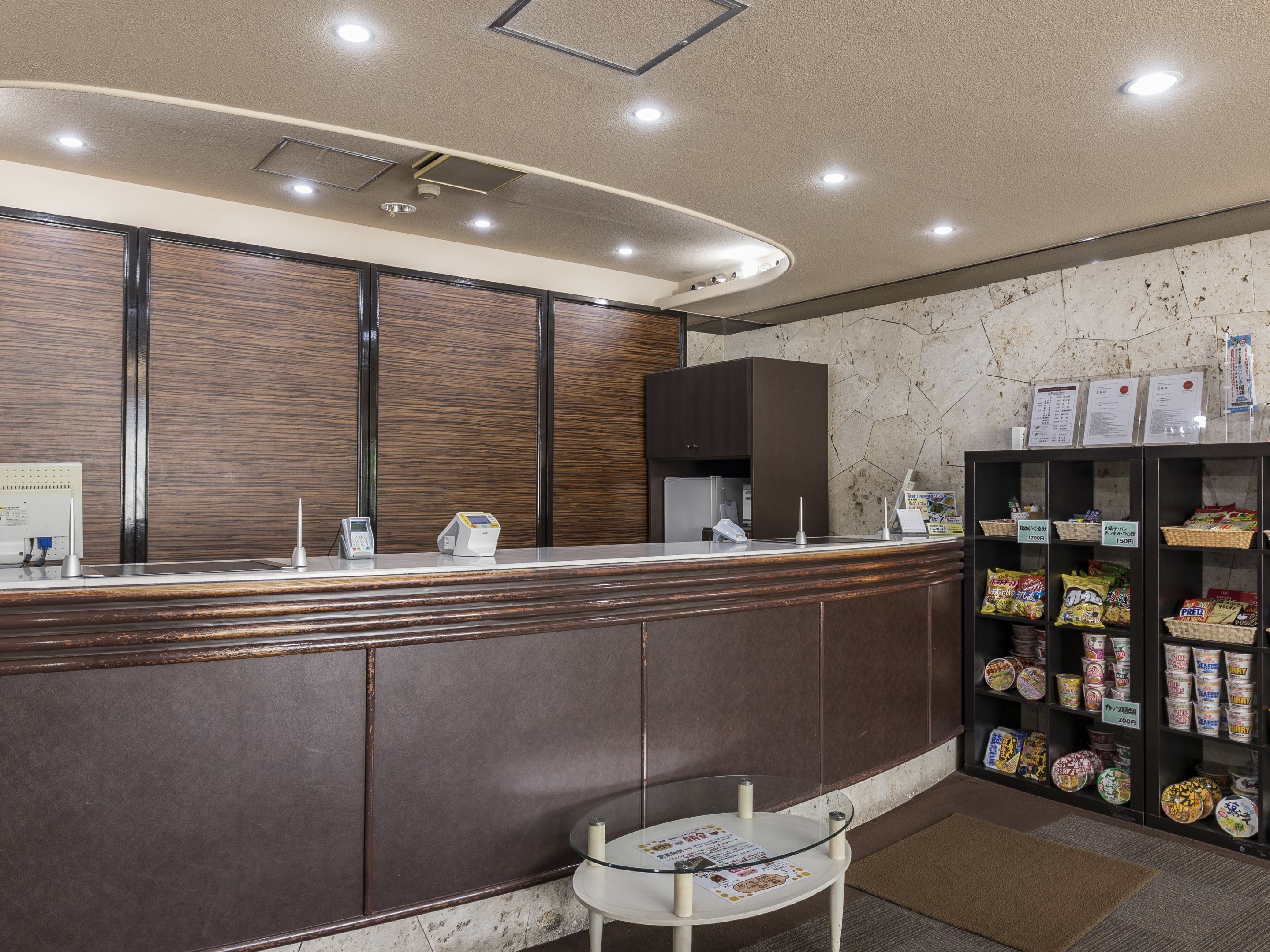 A reception area with a wooden counter, a glass table, and a shelf with packaged snacks.