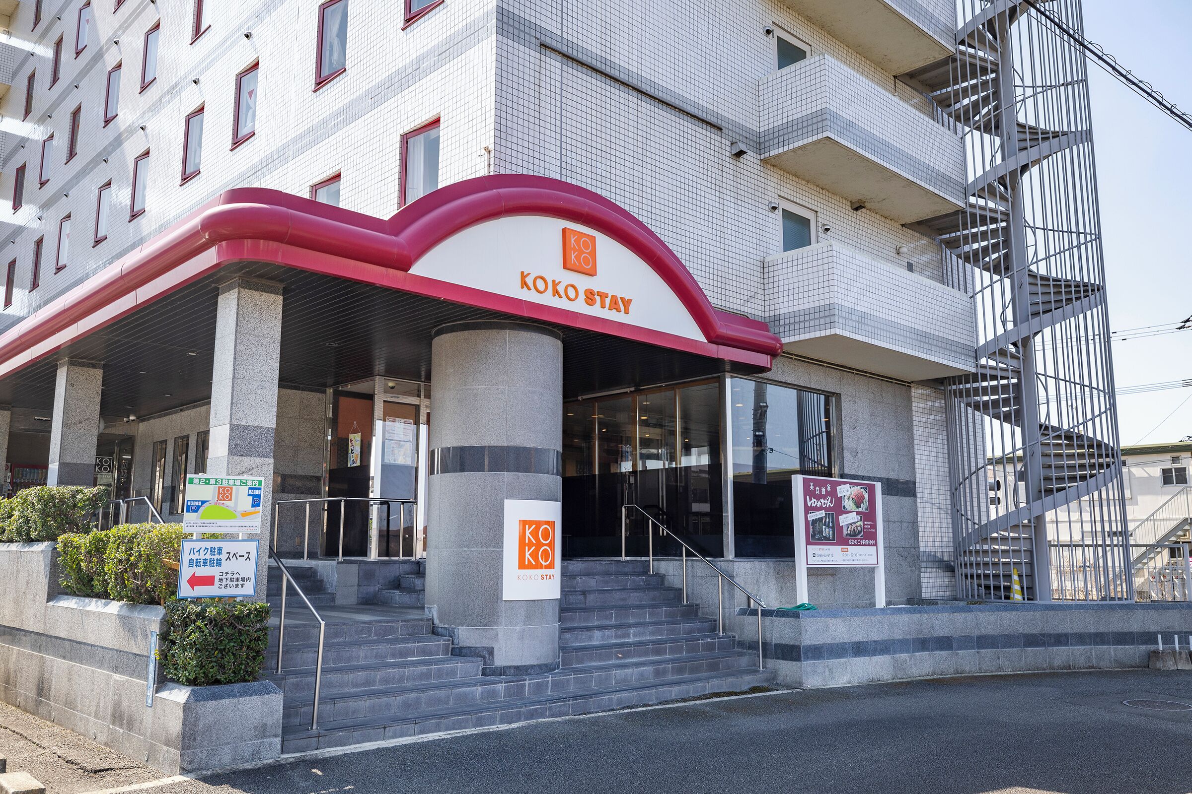 Entrada de hotel con toldo rojo y blanco, una escalera que conduce a la entrada y un letrero que indica el nombre del hotel.