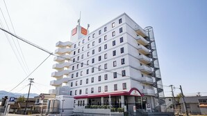 Un hotel de varios pisos con un toldo rojo, un letrero de estacionamiento visible y un cielo despejado.