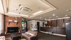 Un hall de hotel con un sofá, un televisor, una recepción y una cocina.