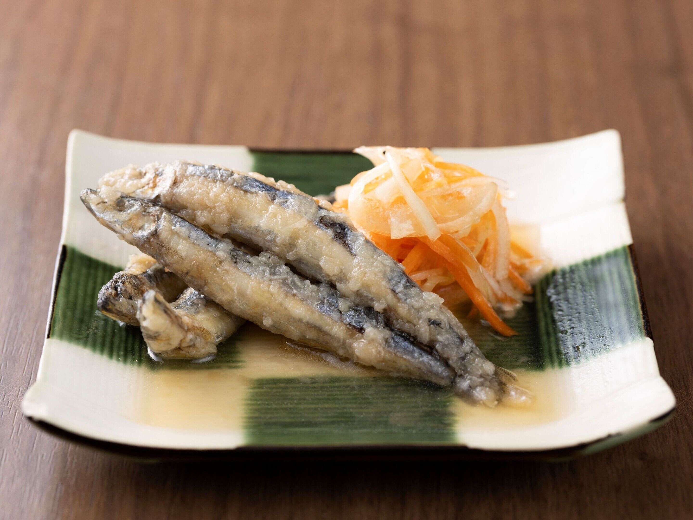 A plate with two fried fish and shredded carrots.