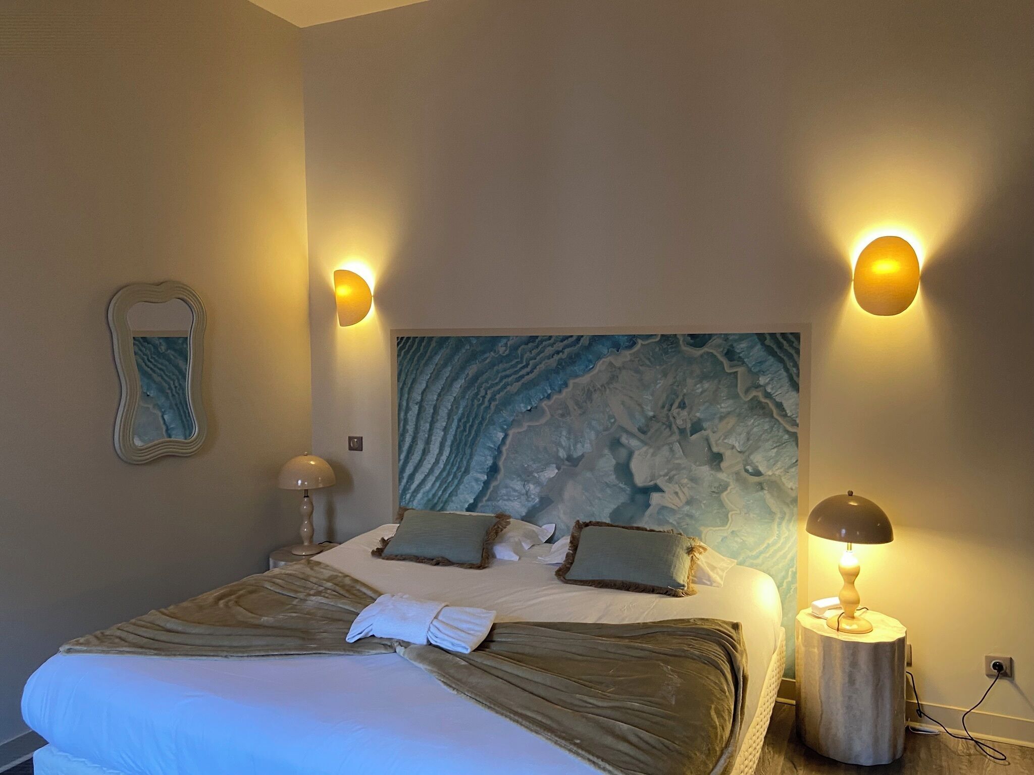 A neatly made bed with a marble headboard, two bedside lamps, and a wall-mounted mirror.