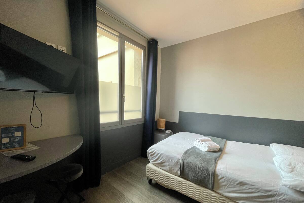A hotel room with a bed, a desk, and a window with curtains.