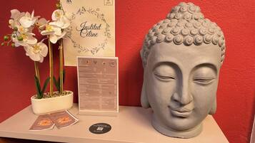 A Buddha head sculpture, a menu, and white orchids on a table against a red wall.