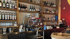A bakery counter with croissants and bread, a coffee machine, and shelves stocked with various bottles of alcohol.