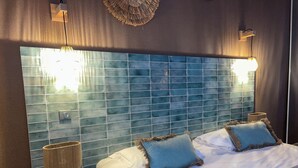 A hotel room with a large bed, two bedside lamps, a round nightstand, and a blue-tiled headboard.