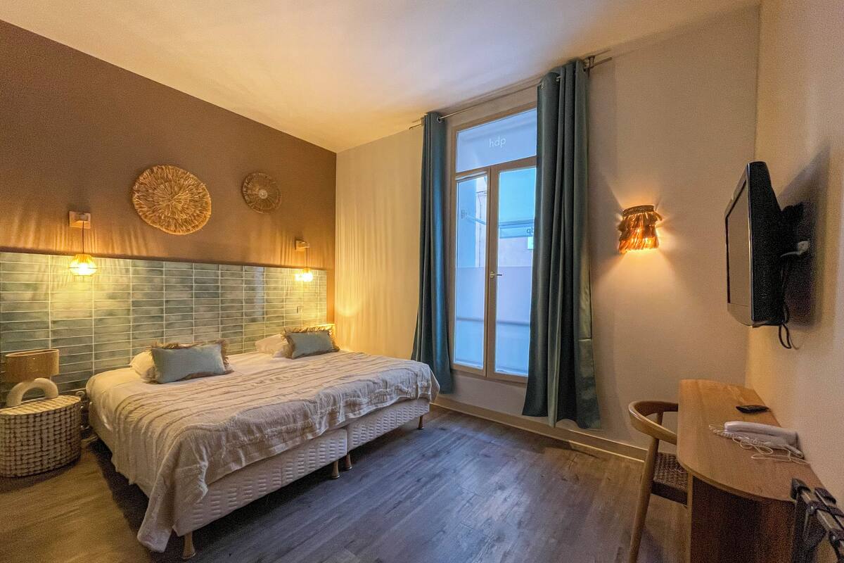 A bedroom with a bed, bedside tables, a mirror, a TV, and a window with curtains.