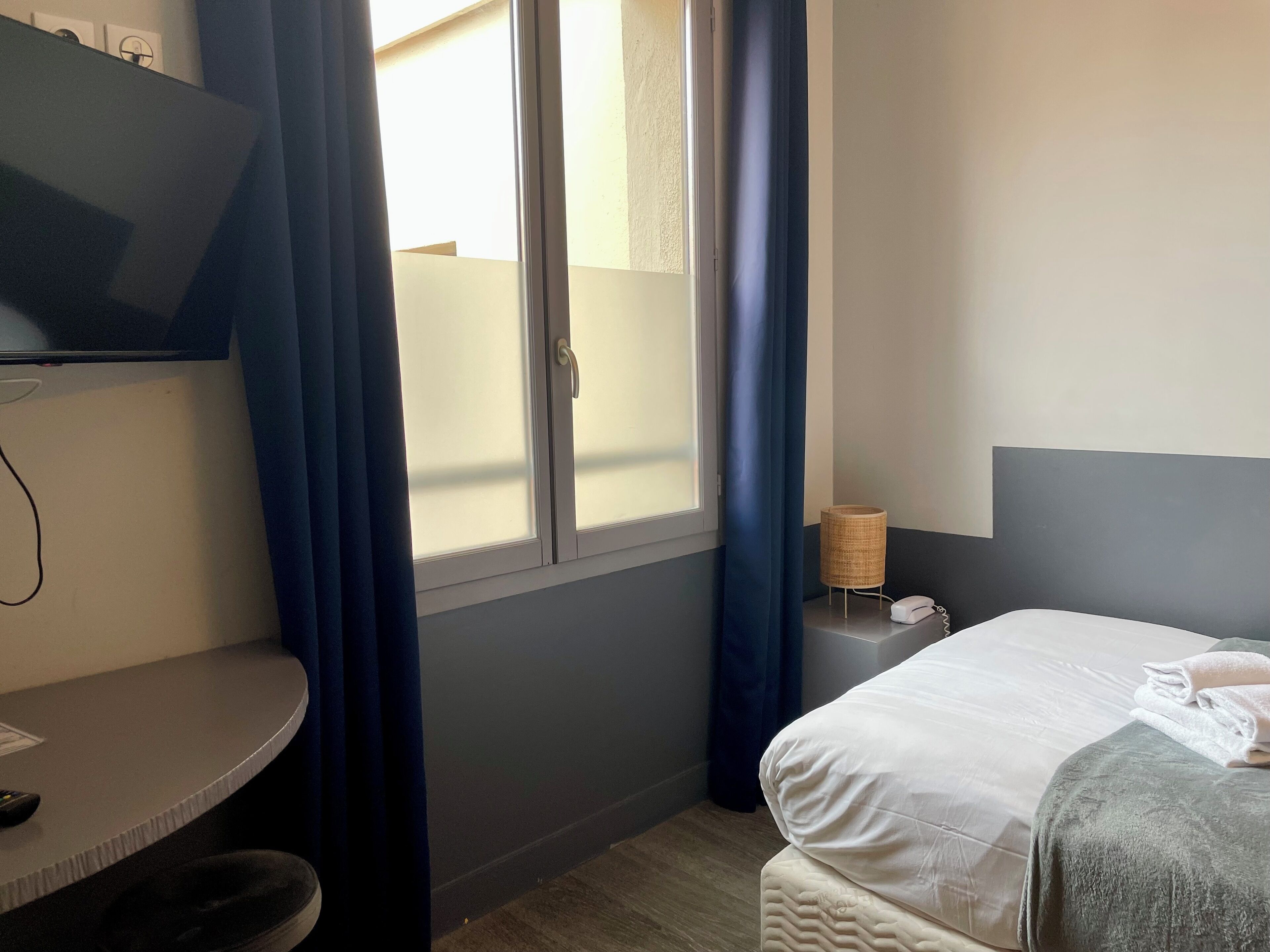 Une chambre d’hôtel avec un lit, un bureau, une télévision et une fenêtre avec des rideaux.
