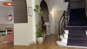 A spacious hallway with wooden flooring, a staircase, and potted plants.