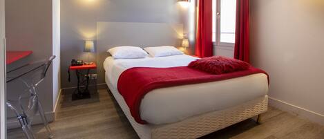 A modern hotel room with a large bed, a desk, and a chair.