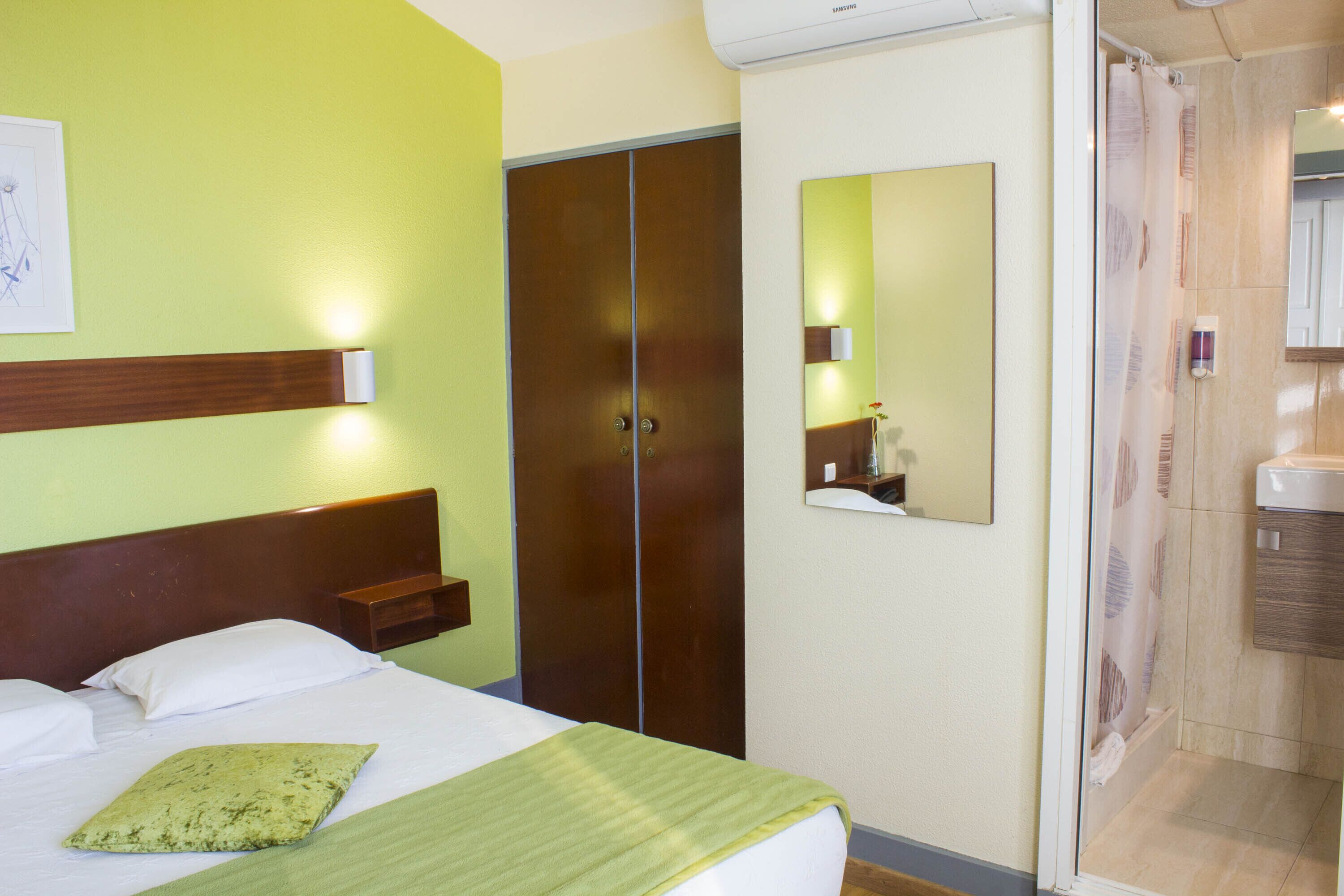 Habitació d'hotel amb llit, armari, bany amb dutxa i mirall a la paret.