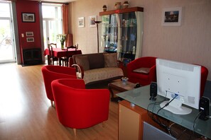 Ein Wohnzimmer mit roten Sesseln, einem Sofa, einem Glastisch und einem weißen Computermonitor.