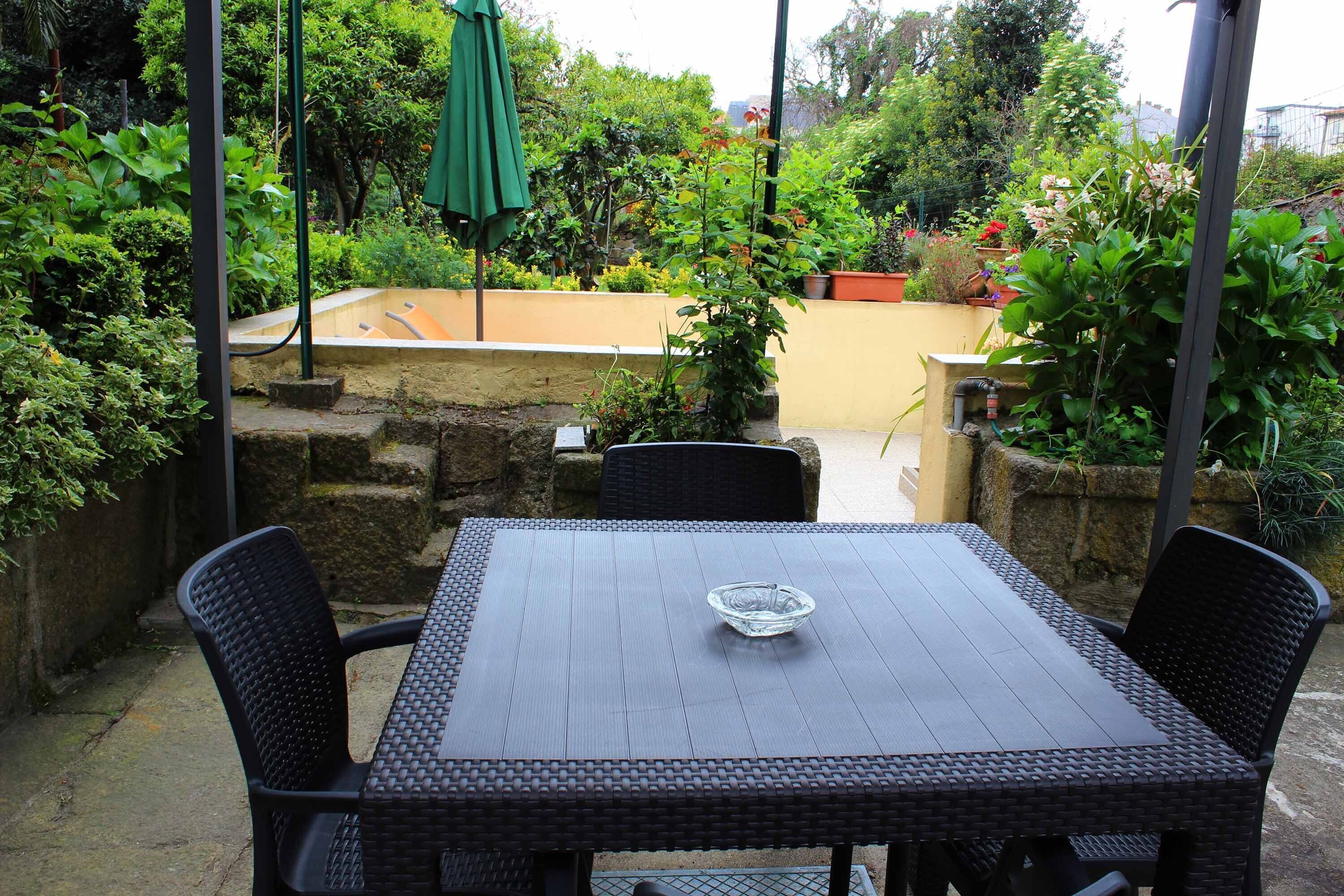 Une terrasse avec une table et des chaises, entourée de plantes et d’un mur en pierre.