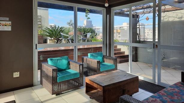 Un balcón con muebles de mimbre, una mesa de madera y vistas a edificios y árboles.