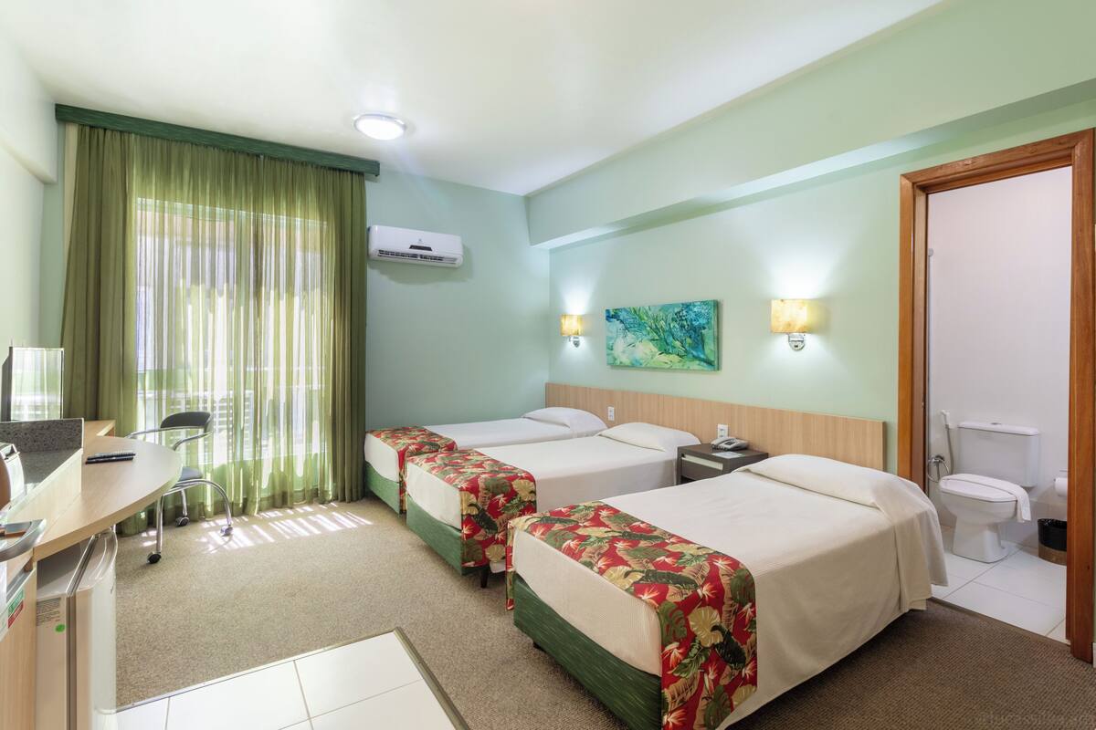 Habitación de hotel con dos camas, un escritorio con computadora, una silla, una lámpara de escritorio y un cuadro en la pared.